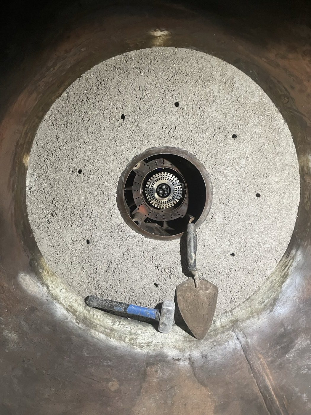 Boiler refractory work around a central burner, with hand tools below.